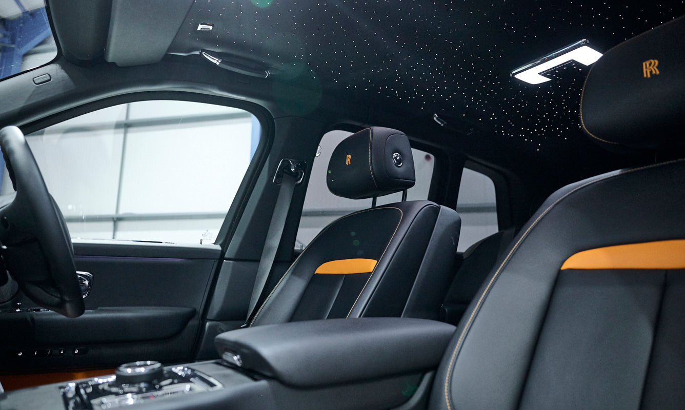 Luxury car interior with black leather seats and starry sky ceiling.