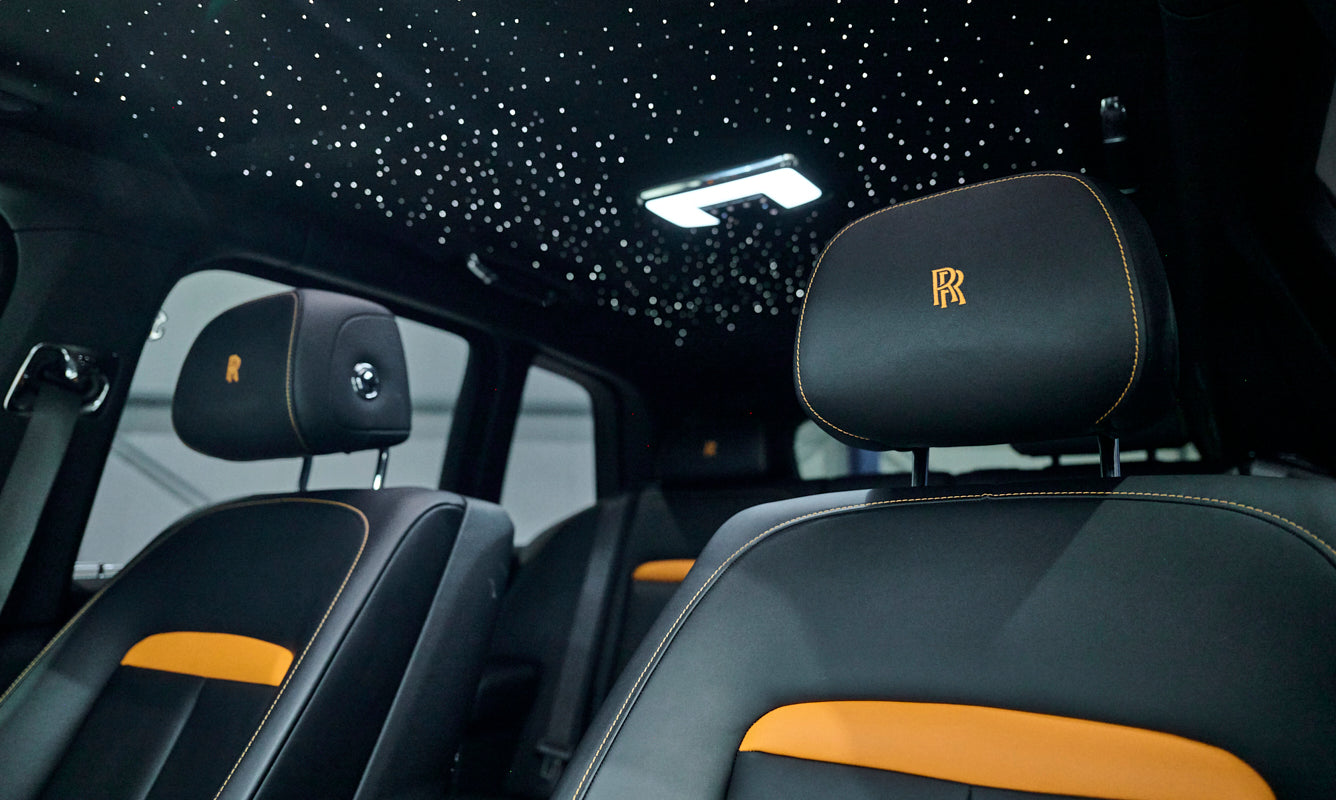 Luxury car interior with starry sky ceiling and Rolls-Royce logo on headrests.