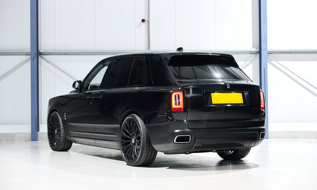 Black luxury SUV parked inside a building with a white floor and blue metal beams.