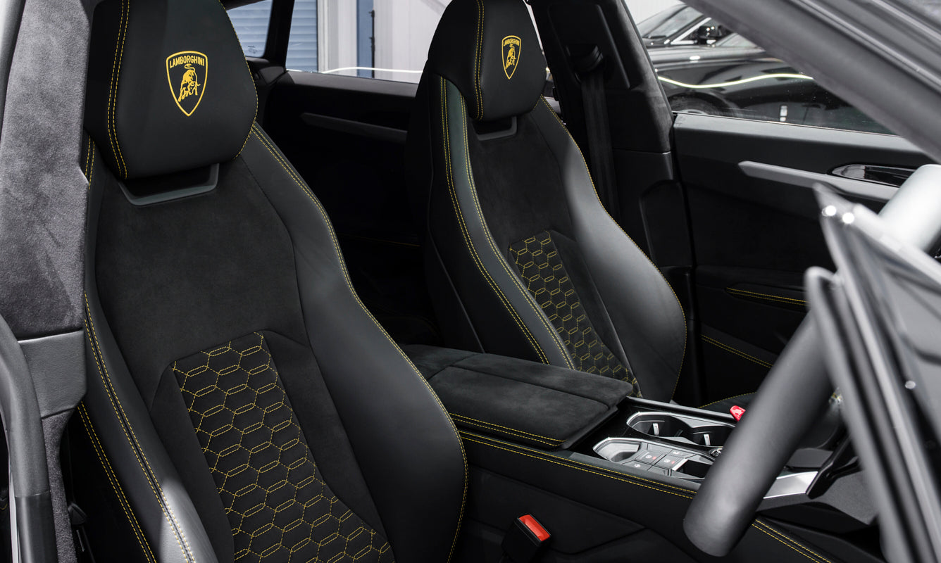 Car interior with black seats featuring Lamborghini logo and branding.